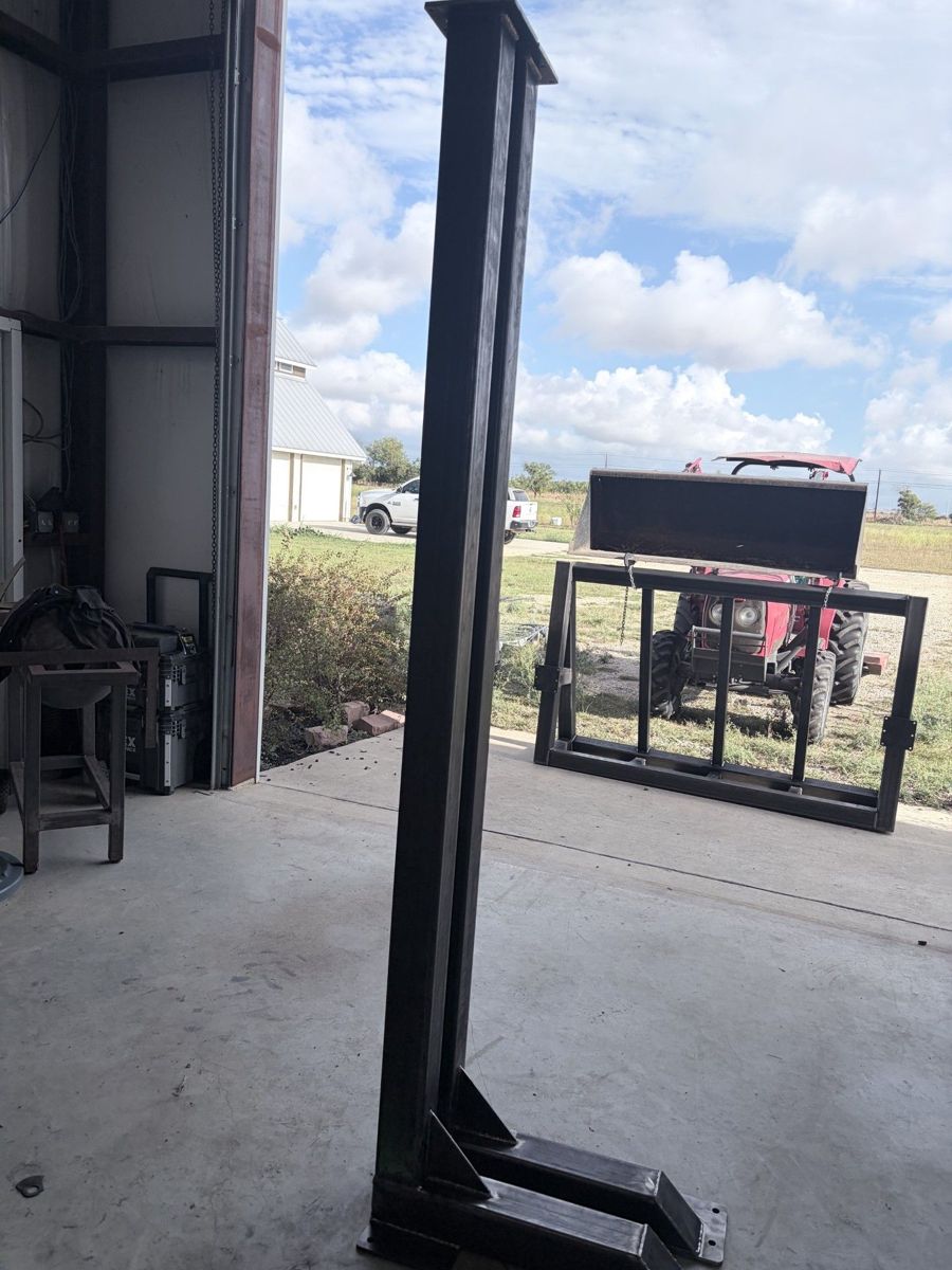 Tall tube-steel column with a gusseted, bolt-down base and a welded frame assembly behind it.