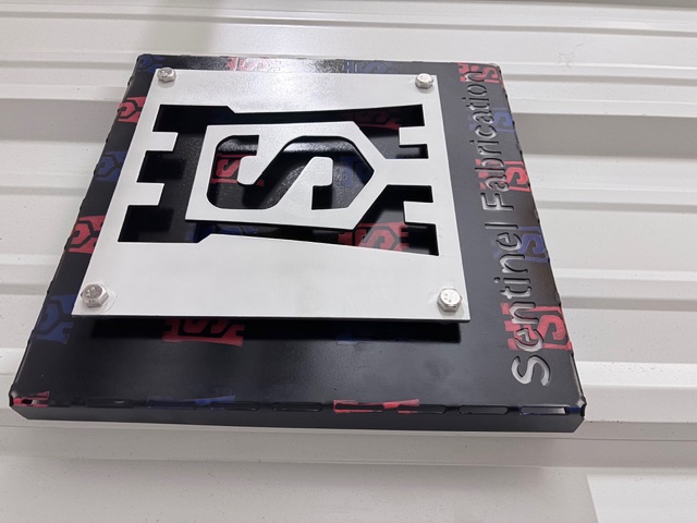 Layered Sentinel Fabrication wall sign mounted on a corrugated wall panel.