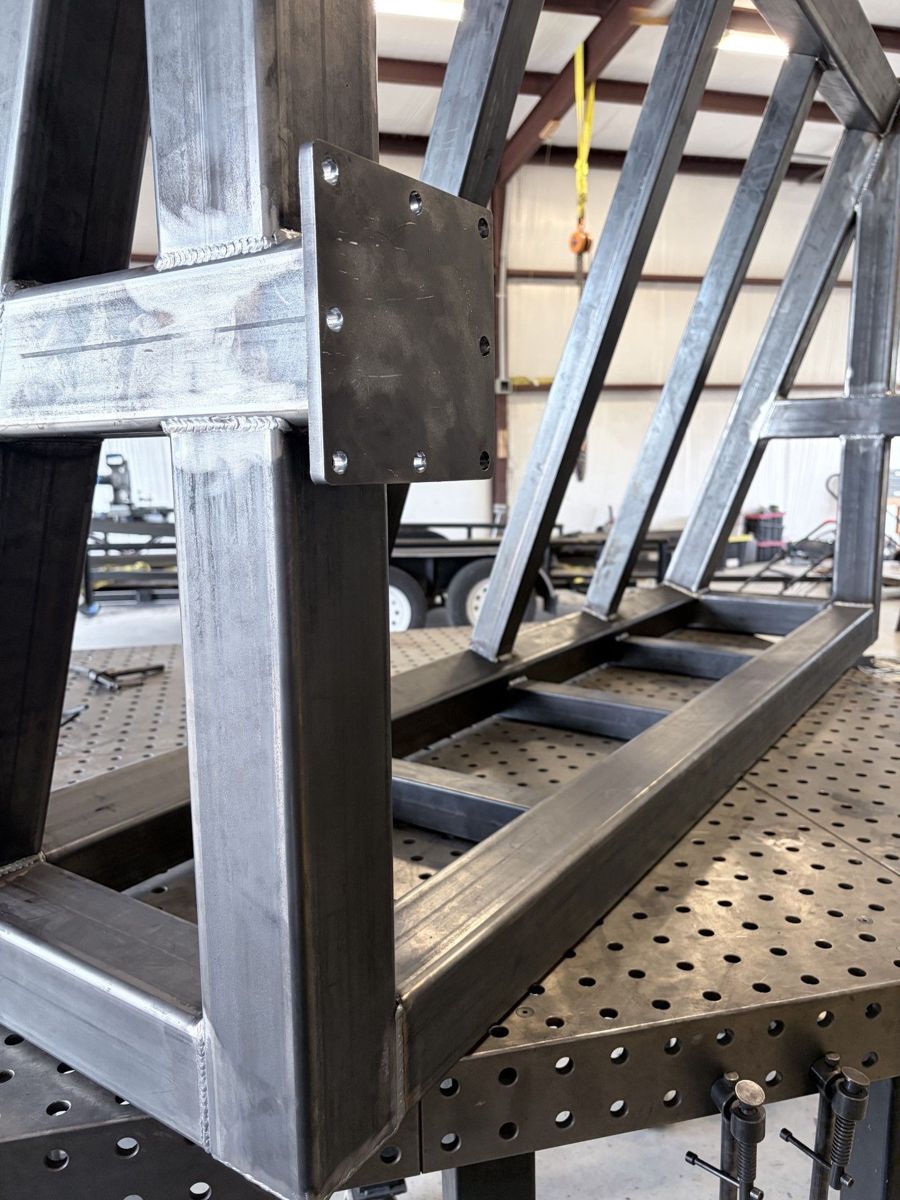 Tube-steel structural frame with a drilled bolt-on mounting plate, squared on a fixture table.