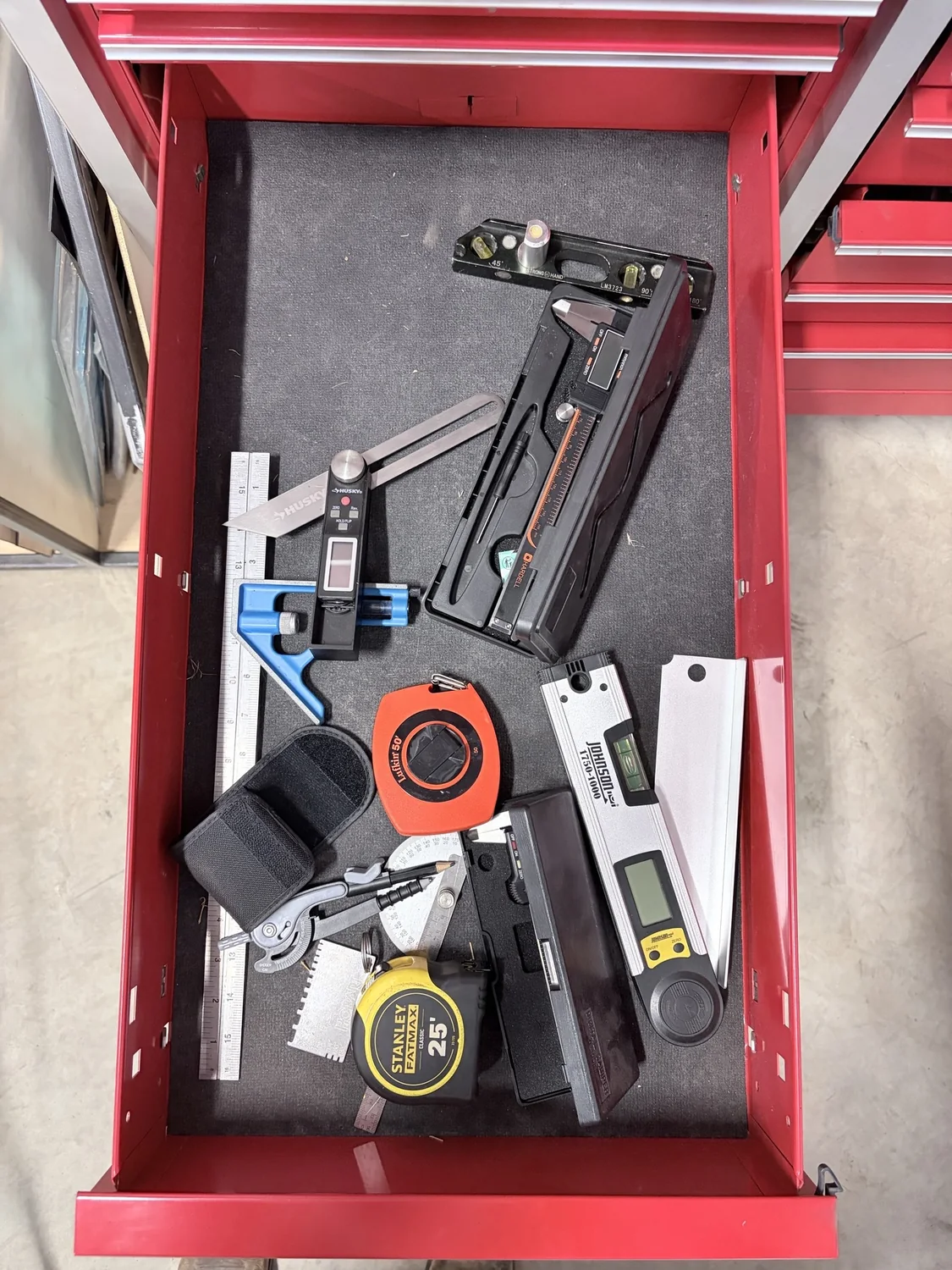 Loose measuring tools scattered inside a red toolbox drawer before a custom foam insert.