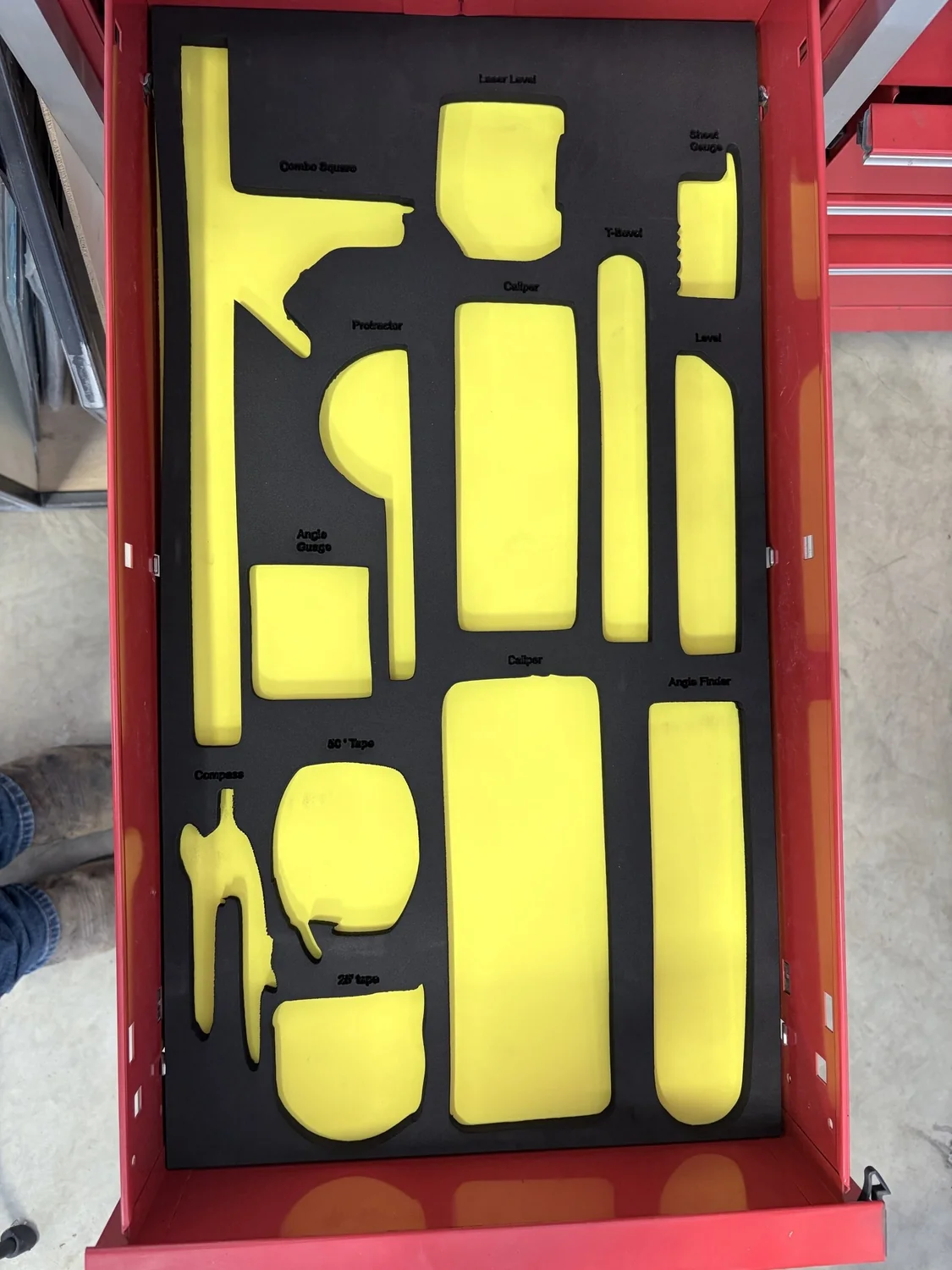 Custom yellow and black foam insert cut for measuring tools inside a red toolbox drawer.